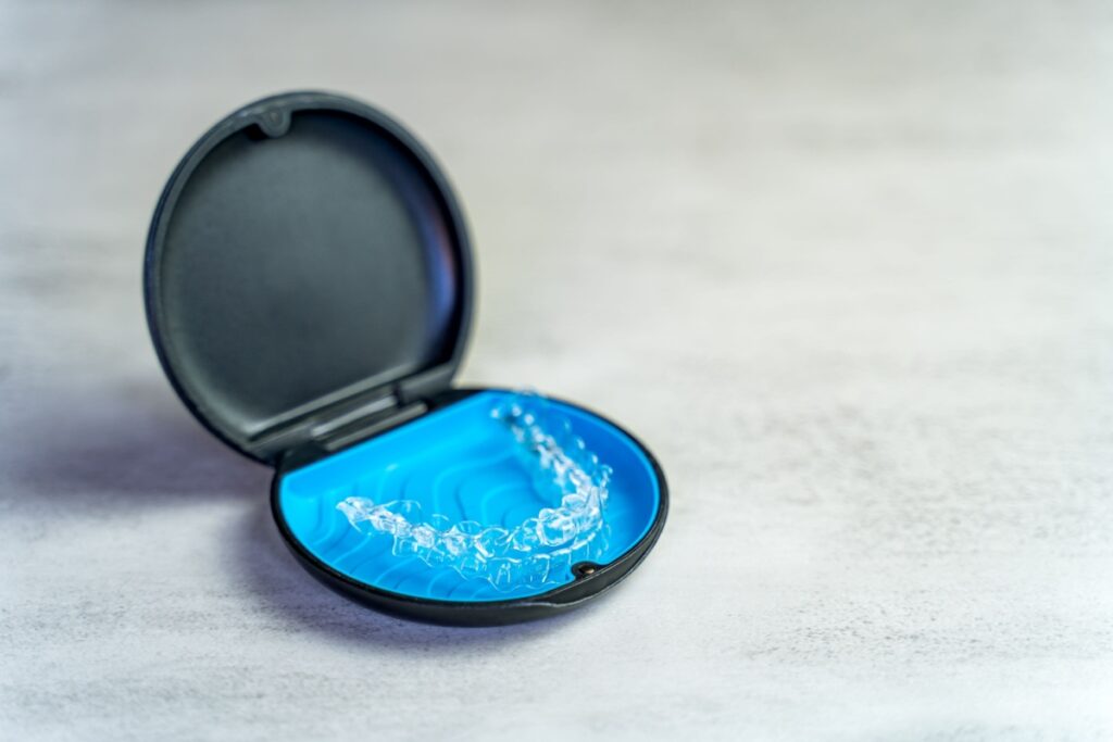Clear Invisalign aligner in an open blue and black storage case on a light surface.