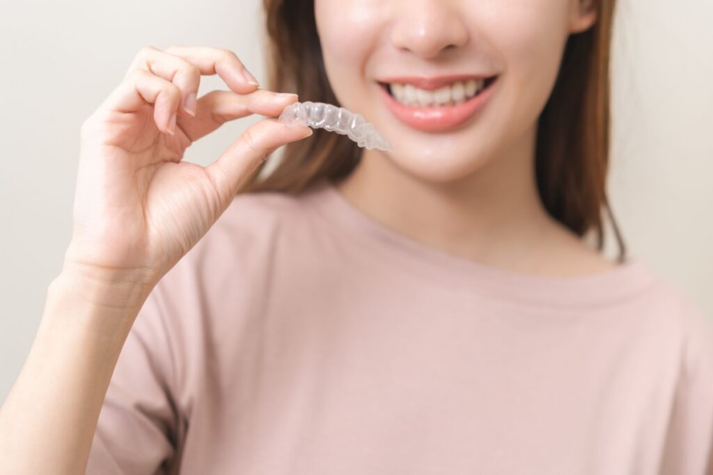 Smiling young woman holding up an Invisalign aligner.