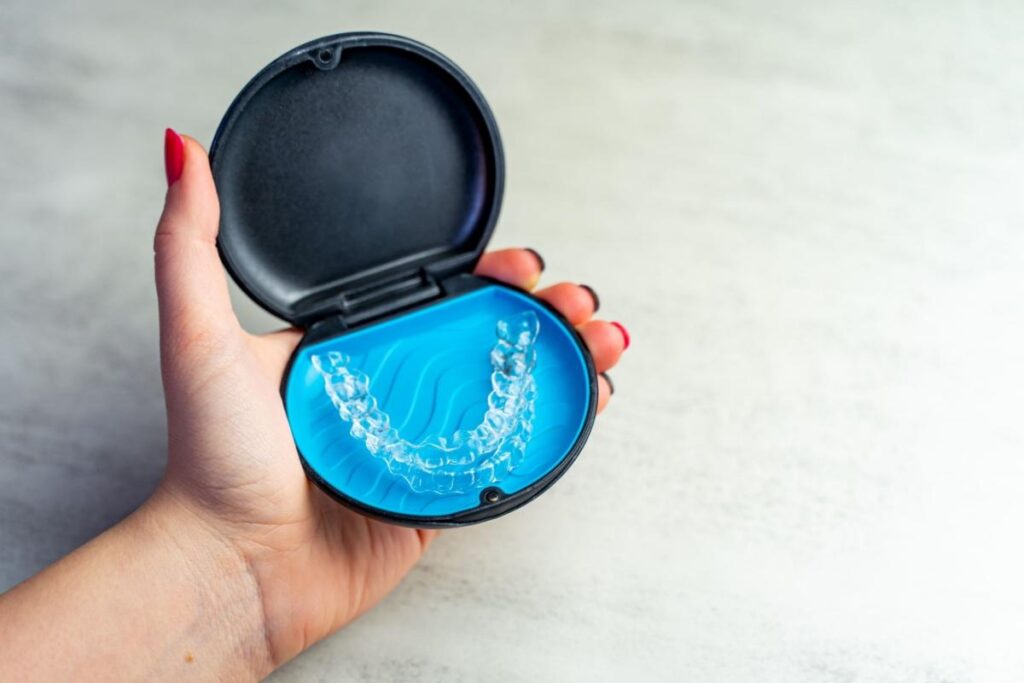 Woman's hand holding Invisalign case with aligner inside.
