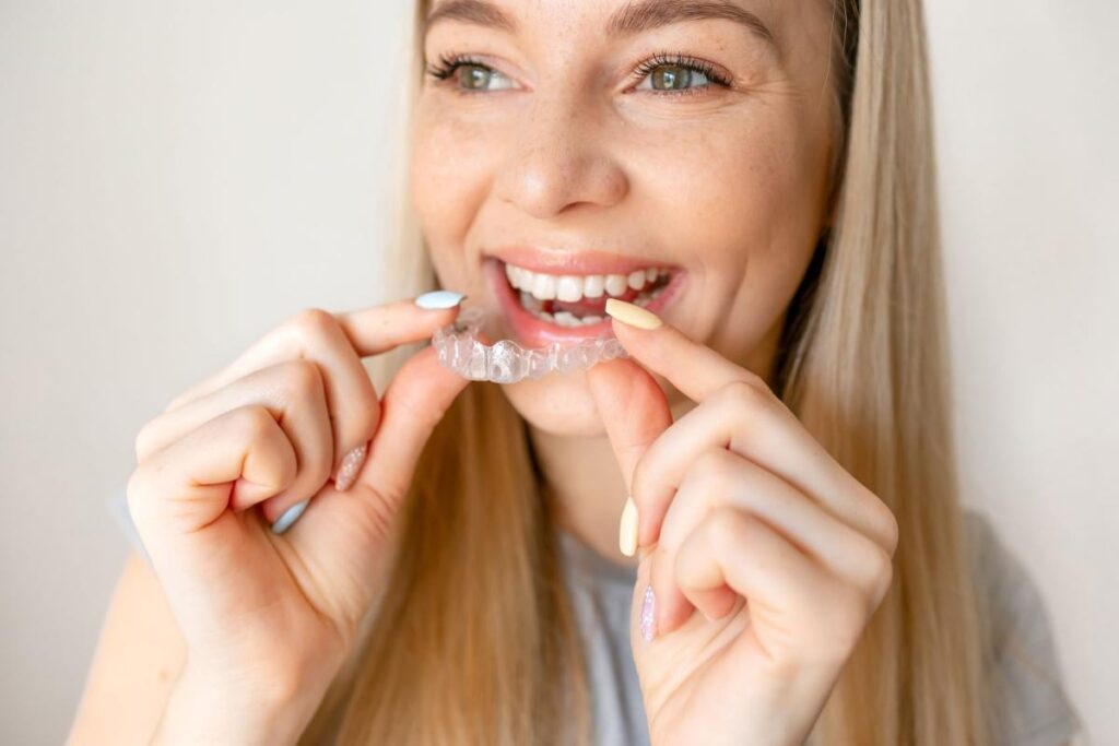 Happy woman putting in her Invisalign on upper teeth.
